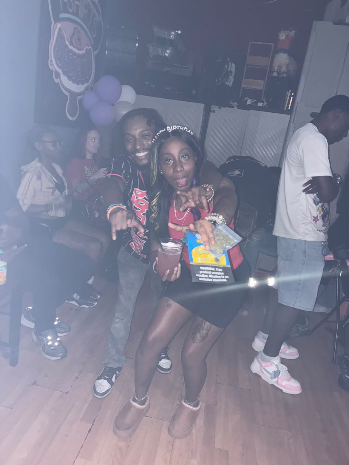 Birthday celebrant posing with a guest in front of purple balloons